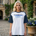 Woman in a white and navy raglan tee with a "TENNESSEE HEBREW" graphic and state silhouette, standing in a courtyard with ivy-covered walls.